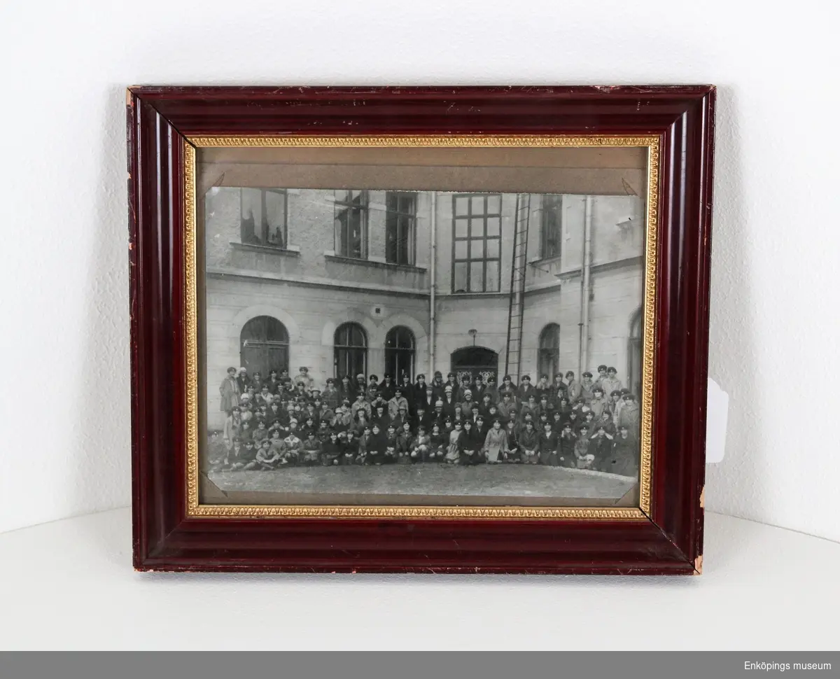 Tavla med inramat fotografi.
Fotografiet föreställer flickor från Elementarskolan för flickor, Enköping, läsåret 1928–29. De står förmodligen på innergården vid gamla Sparbankshuset.
Dr. Ernst Westerlund var initiativtagare till Elementarskolan för flickor. Skolan startades den 1 september 1885. Dr. Westerlund donerade skolmaterial, möbler, hyrde skollokal och donerade pengar till skolan. Han var även hälsoansvarig på skolan och gav eleverna kostnadsfri sjukvård. Skolan lades ned 1935.
Den sista bilden visar ett tidningsurklipp från Enköpings-Posten den 8 juni 1886 där dessa fakta framkommer.