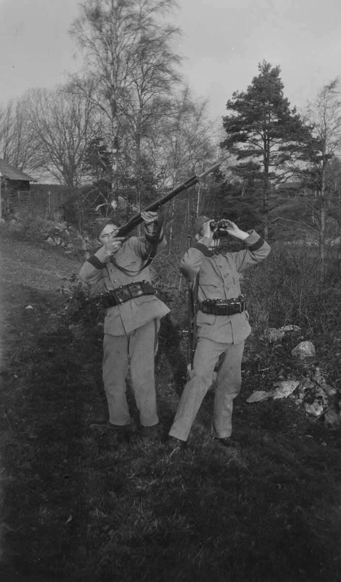 Två frivilliga luftbevakare från landstormsregemente L 2 i Dalsland under beredskapstiden. Mannen till vänster siktar med gevär mot skyn. Mannen till höger spanar i kikare mot skyn.
