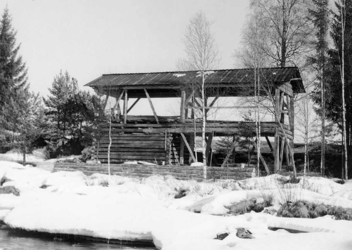 Oppgangssaga fra Andrå i Ytre Rendalen, fotografert etter at den ble gjenoppført ved Glommas bredd på det som da hette Norsk Skogmuseum i Elverum.  Fotografiet er tatt fra vest, antakelig fra isen på elva, mot ei av langsidene på saghuset.  Vi ser hvordan bygningen er utført i to etasjeplan.  Den ytre delen av det nedre planet har en åpen, stolpebåren konstruksjon, mens den øvre består av ei luftig, rektangulær tømerkasse.  Oppå dette funamentet er det lagt et par laftete omfar med bygningstømmer, som også tjener som fundament for golvet i saghuset.  Oppå de laftete omfarene igjen er det en bærekonstruksjon for raft, røster og tak som består av stolper og skråstivere.  Saghuset har bordtekket saltak.  I forkant av bygningen ser det ut til at det er lagt en skådam (skjerm) av tømmer parallelt med husets retning.  Bygningen er plassert i en elveskråning, omgitt av bjørke- og grantrær. 