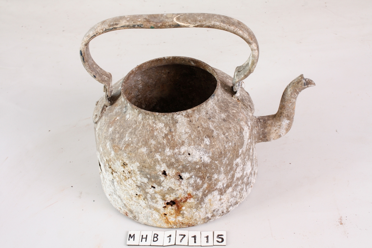 Kaffekjele i hvitt metall med helletut og hengslet håndtak. Hvert hengsel er festet til kroppen med to nagler, og til håndtaket med én nagle. Håndtaket er ikke lenger bevegelig, og står rett opp. Helletuten er festet nederst på kroppen, og er svakt avsmalnet og bøyd opp og utover. Kjelen mangler lokk. Kjeleformen er konisk med innsvinget topp. Metallet er matt, med flere ujevne korrosjonshull i den ene siden. Det er små sorte, hvite og grønne malingsflekker på overflaten.

I kjelen ligger diverse små gjenstander.
- 24 jernspiker i ulike størrelser, flere er trolig belagt med sink.
- En ringklemme med skruegjenger, trolig jern belagt med sink.
- En trekork.
- Tre små jernbiter, uidentifisert.
- Tre ringer/deler av ringer, av jern og kobber.
- Fire jernmuttere, ulike størrelser.
- En blålig taustump, trolig bomull.
- En jernsylinder med skruegjenger.
- En skruebolt av jern.
- En kobbersylinder med hull i sidene og et buet jernlokk i en ende.
- Flere fastrustede spiker og muttere.