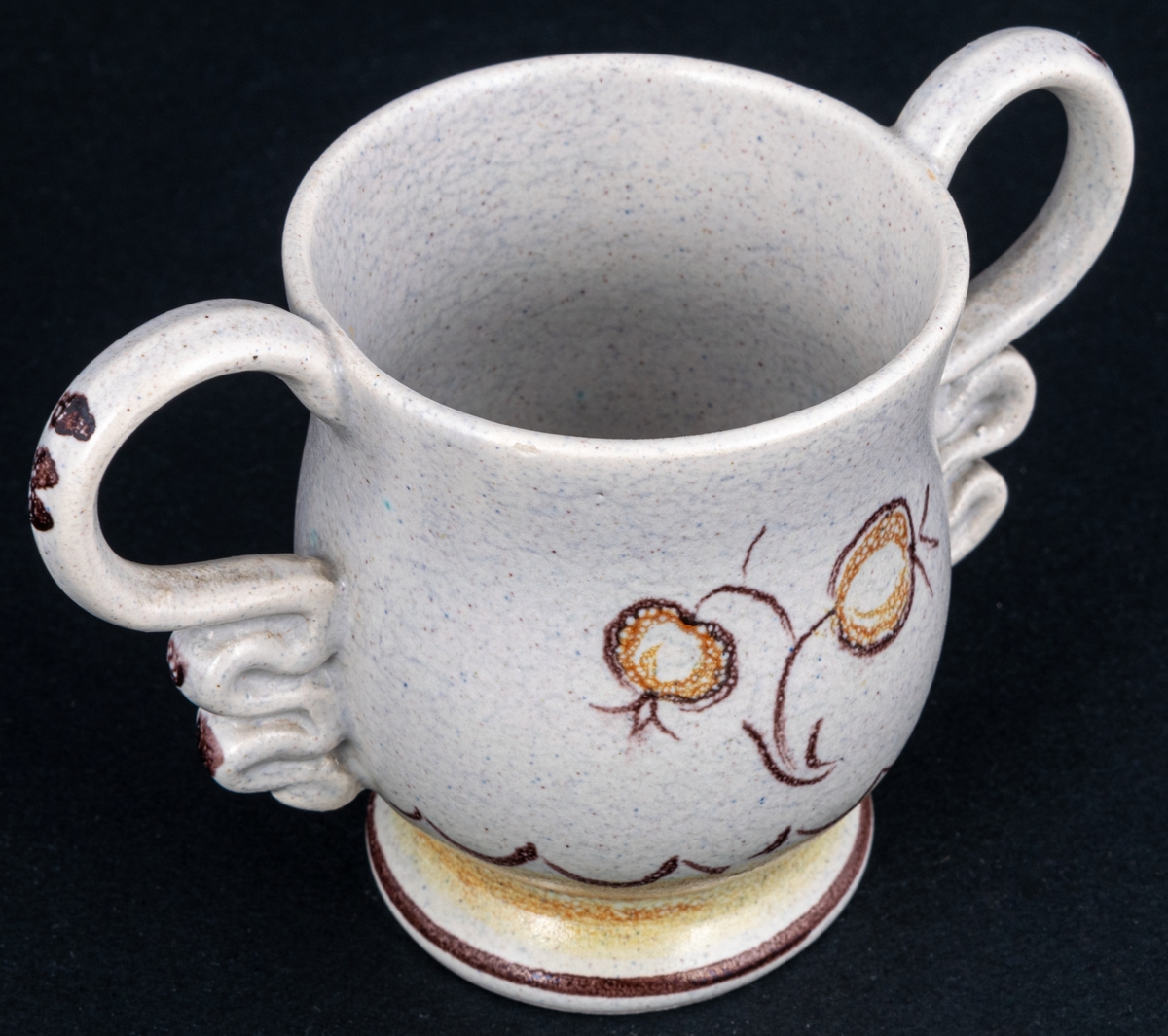 Bägare av lergods. Bo Fajans, design Eva Jancke­Björk. Grå S­svängd med stora hänklar, ljus- och mörkbruna partier nedtill samt dekor av en blomma.