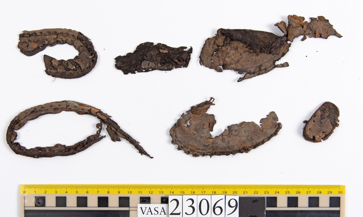 Dokumentation 1996:
Delar och fragment av sko: en skobotten samt ett fragmentariskt ovanläder, tre bitar av ett filtliknande material, ett 15-tal fragment av bottenläder samt sex mindre fragment av trä.
Skobottnen har kvarsittande tråd och träpligg. Yttersulan är ritsad. Klacken består av fem klacklappar som är placerade mellan ytter- och innersulan. Innersulans läder är mycket kraftigt, ca 6 mm tjock. Ovanlädret är sprött och fragmentariskt samt har blå och rostfärgade utfällningar.

Text in English: 
Various parts and fragments of a shoe, consisting of a sole with fragments of vamp (upper leather), three pieces of a felt-like material, some 15 fragments of sole or bottom leather and six smaller fragments of wood.
There are remains of thread and wooden pegs on the shoe sole. The outsole is channeled. The heel is made up of five heel lifts placed between the insole and outsole. The leather of the insole is very thick, ca 6 mm. The upper leather is fragile and fragmentary, and has blue and rust-coloured precipitations.

Dokumentation 2022:
Skobotten och delar av ovanläder till en öppen randsko. Tillverkade i getskinn av god kvalitet. Skapades på en rak läst och bars på höger fot. Klacken som är lagad med en läderlapp under sulan. Inga dekorationer. Det finns tecken på delaminering. Fragment från en stickad strumpa hittades inuti skon. Det finns lagningar med träpligg på sulan och hälen. Skobotten hör ihop med fyndnummer 23070.
För mer information, se Länkade filer: Uppritning

Text in english:
This is the bottom unit and upper fragments of an open shoe, made of goatskin leather of good quality, of randed construction with a patch heel, made on a straight last and worn on the right foot, with no decorative features. The bottom unit pairs with 23070. There are signs of delamination and fragments of a knitted stocking were found inside the shoe. There are pegged repairs to sole and heel.
For more information, go to Länkade filer: Uppritning