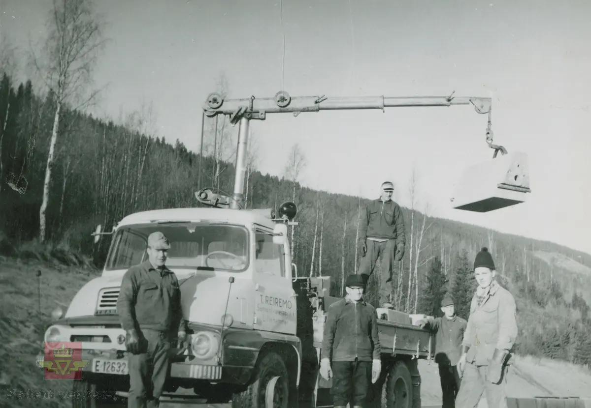 Nedsetting av kantstein høsten 1965.  "T. Reiremo Sementvarefabrikk Lillehammer, " Foran lastebilen, med kjennetegn E-12632, står fra venstre lastebilkjører Morken, Sigurd Sørum og Dag Solheim lengst til høyre. Bak er Hans Johansen og Halvard O. Sveen. 
Lastebilen er en engelskbygd Ford Thames Trader FC, som var i produksjon 1957-65. FC sto for Forward Control/dvs. bulldog/halvbulldog, med et meget karakteristisk design av frontpartiet. Se: Asbjørn Rolseth: Norsk Lastebilleksikon bind II (1940-1990) s. 132-134. Et ekstra poeng: nedre del av grillen er tydelig inspirert av amerikansk Ford lastebil 1953-56, kfr. bilder Rolseth s. 127. Opplysninger om kjøretøyet fra Ivar E. Stav.