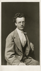 Porträttfoto av en ung man i glasögon, klädd ljus tweedkosty