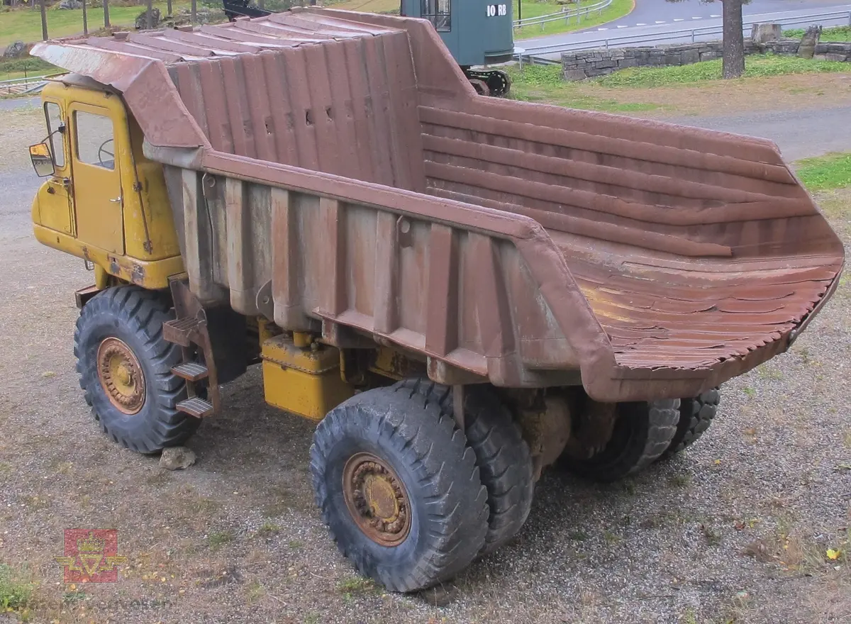 35 tonns gul dumper med 6 hjul, 2 akslinger. Tvillinghjul på bakaksel. 6-sylindret 14,6 liters Caterpillar dieselmotor som yter 400 hk. Dumperkassen har et volum på 17,8 m³. Skiltplater med serienummer 99F986 plassert på rammen og motoren. Metallplater fra produsenten med smørekart og advarsler. Hytte og motordeksler er i glassfiber. Dumperens toppfart er på 69 km/t.