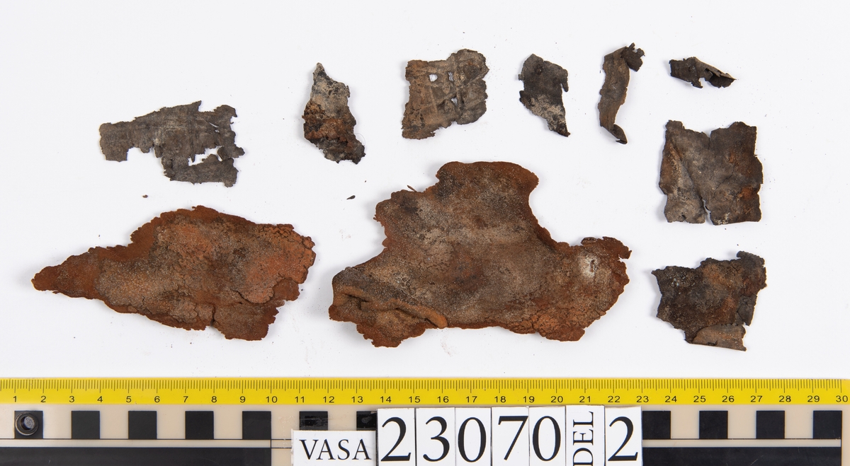 Sko.
Inuti skorna hittades även fragment från olika textilier som ursprungligen varit ett par strumpor. Idag sitter ett stickat fragment av ull fast i vänsterskon (23070) med avigsidan uppåt. I fyndet finns även en mängd lösa stickade fragment som idag är mycket korroderade och vissa helt mineraliserade av järn vilket har gjort textilen stenhård och därmed oerhört skör (23070a-c). Utifrån minskningar som några små fragment har så har det varit möjligt att rekonstruera strumpans tå. Genom att pussla ihop fragmenten som ursprungligen har suttit ihop har det på så vis gått att avgöra hur strumpans tå har varit konstruerad. Då textilen är så fragmentarisk är det inte möjligt att avgöra hur resten av strumpan har sett ut eller varit konstruerad. Däremot så finns det fragment av ett kypertvävt tyg av ull som på vissa ställen ligger dubbelt med det stickade 23070c). Ett av dessa fragment har stelnat i formen så som den suttit på fotens främre del inuti skon. Detta fragment täcker delvis det stickade tyget och har dessutom spår av kaststygn längs en kant. Så som det vävda tyget är placerat på det stickade tyget pekar på att man använt det som lagningslappar till sina stickade strumpor. 
I fyndet finns det även korroderade järnklumpar, ett tuskaftsvävt tyg av ull och rester av ett grovt bastfibergarn och två mindre läderfragment (23070d-f). Det är möjligt att även dessa har tillhört strumpan och/eller skon.

För mer detaljerad information från textildokumentationen (år 2022) se länkade filer.

Skodokumentation 2022:
Ovanläder. Tillverkad i getskinn av god kvalitet. Hör ihop med fyndnummer 23069 (Yngves skor). Tillverkades på en rak läst och bars på vänster fot. Inga dekorationer Det finns stygnhål som visar att det funnits invändiga förstärkningar (men förstärkningslappen saknas). Det finns delaminering men inga lagningar.
För mer information, se Länkade filer: Uppritning

Text in english:
This is the upper of a shoe of more “extreme fashion”, made of goatskin leather of good quality, probably made on a straight last and worn of the left foot, with no decorative features. The upper couples with 23069, together composing Yngve’s shoes. There are internal reinforcements missing from the upper and delamination, there are no repairs.
For more information, go to Länkade filer: Uppritning