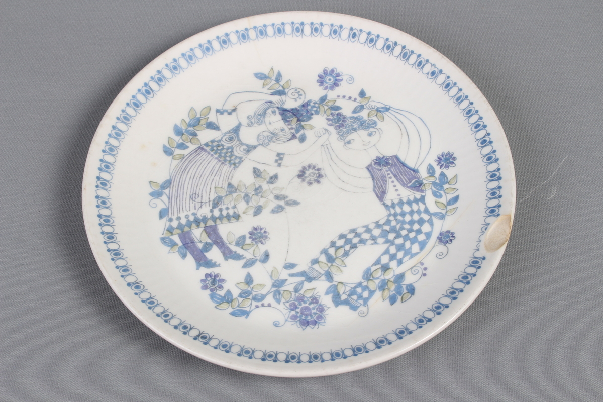 Tallerkene er dekorert med et bilde av en mann  og en kvinne som har blader og blomster på seg og rundt seg. De to menneskene er glade og de danser i blader og blomster.