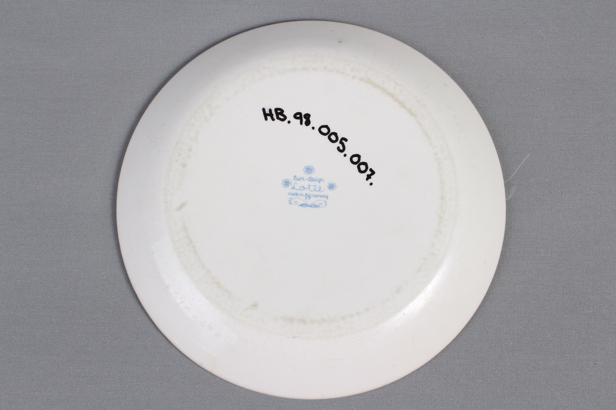 Tallerkene er dekorert med et bilde av en mann  og en kvinne som har blader og blomster på seg og rundt seg. De to menneskene er glade og de danser i blader og blomster.