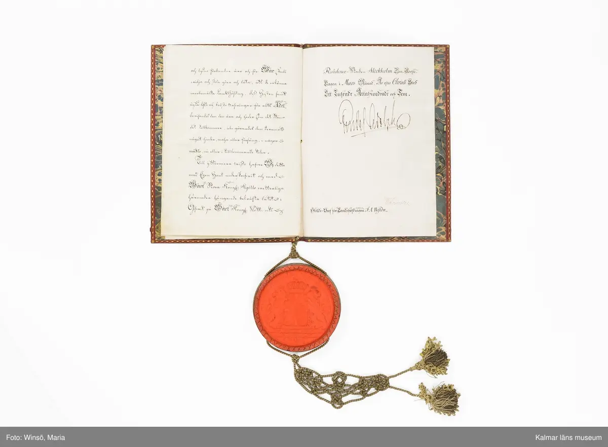 KLM 16024. Sköldebrev, adelsbrev, läder, papper, färg, metall, textil. Sju sidor med handskrift på pergament, inbunden med gul och grön tvinnad snodd med tofsar. På sida tre kolorerad bild av adelsvapnet. Pärm i rött skinn (chagrinband). Guldtryck fram och baksida med Gustaf IV Adolfs krönta monogram samt dekor i guld runt pärmens kanter. Vidhängande lacksigill med svenska riksvapnet i försilvrad kapsel.