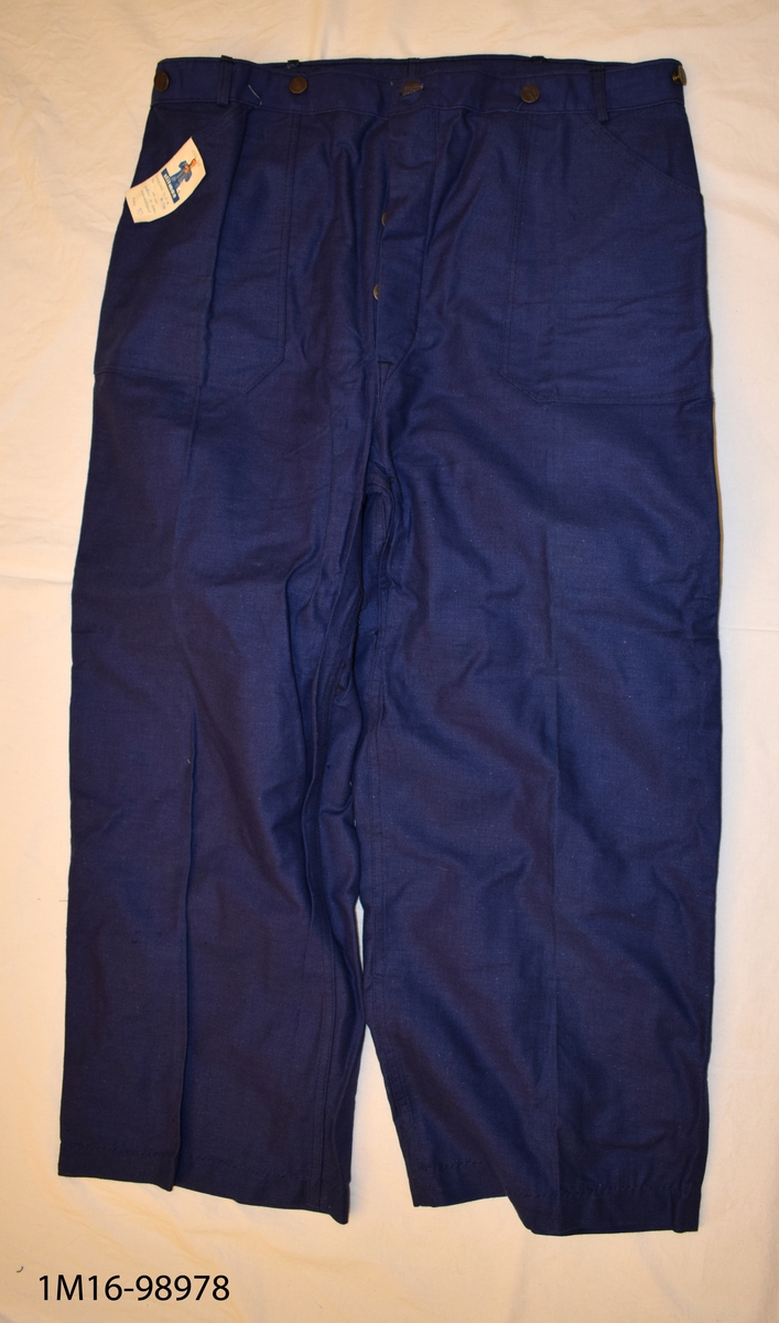 Herrbyxa - blå med två stora fickor fram. Bakficka. Sleif bak med metallspänne. Metallknappar i midjan för hängslen. Gylfen knäpps med fyra metallknappar. 
Upplagda byxben (för hand) Nya.
Märkeslapp medföljer med texten: Storlek 52. Inköpspris: 7.50 Kr.