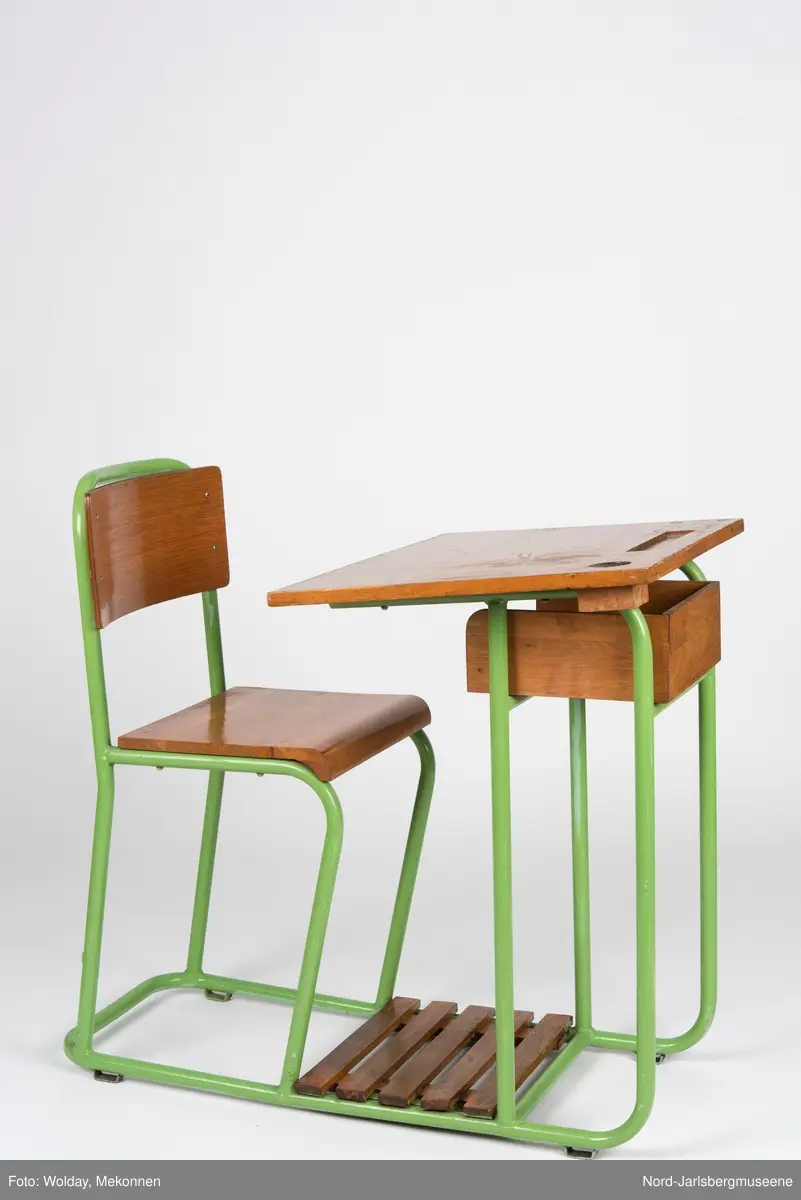 En sammenhengende stol-bord til en person. Stol- og bordbein av metallrør, sete, ryggstø og bordplate av finer.