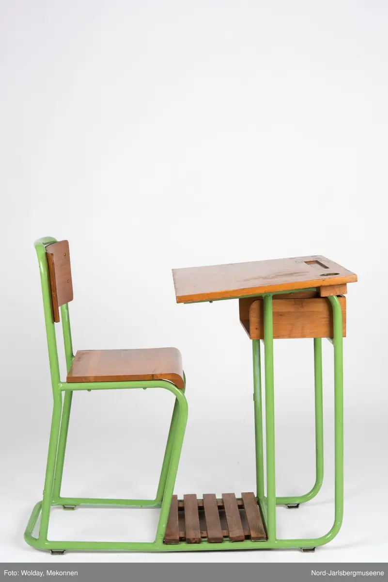 En sammenhengende stol-bord til en person. Stol- og bordbein av metallrør, sete, ryggstø og bordplate av finer.