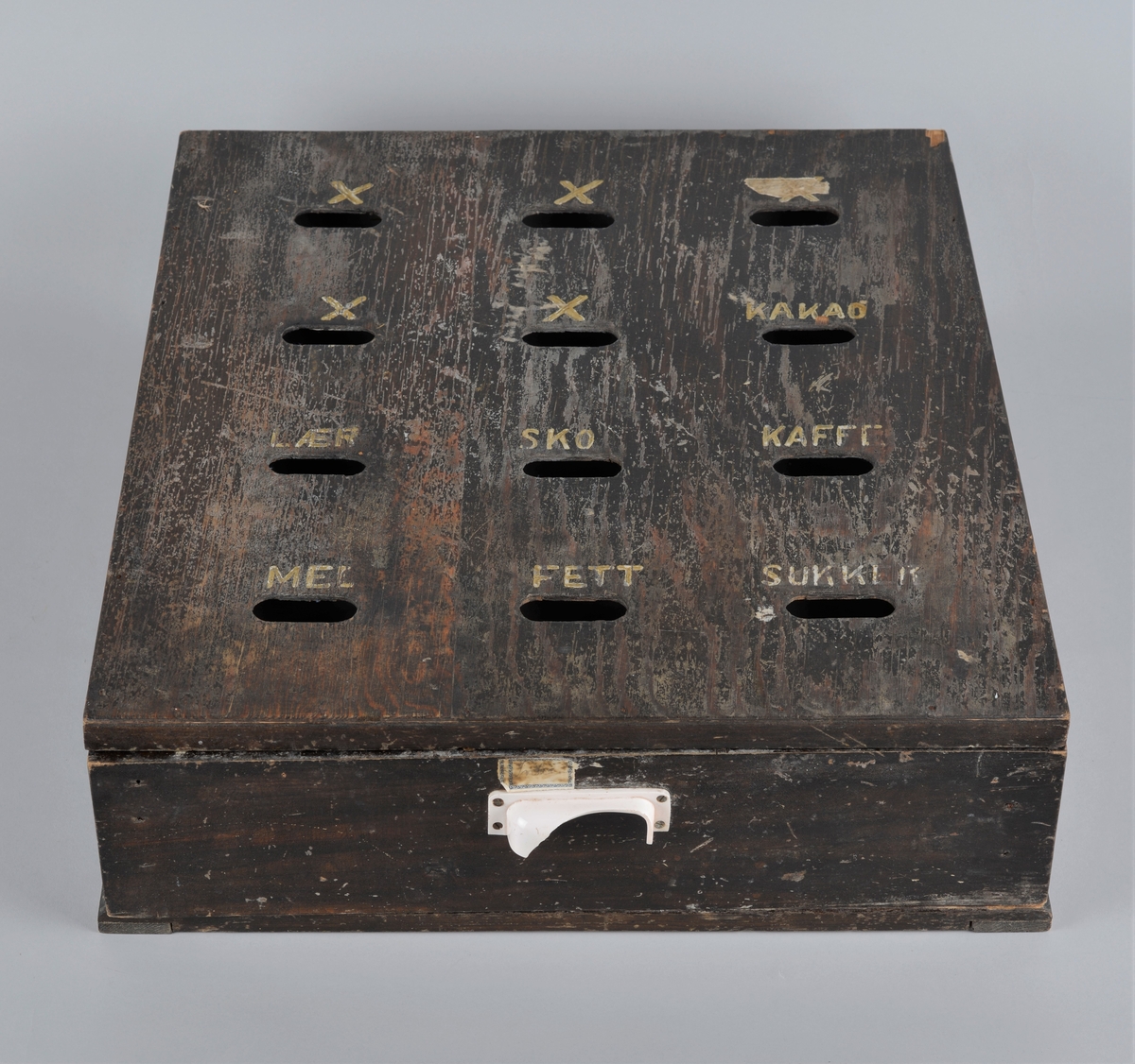 Trekasse for oppbevaring av rasjoneringskort, brukt under og etter andre verdenskrig.
Kassen har en uttrekkbar skuff med flere rom som passer til åpningene i fronten. Håndtaket på skuffen er delvis knust.
Kassen har 12 åpninger i 4 rekker, der det er påmalt tekst: 
1 rekke: X -  X - X 
2 rekke: X - X - kakao
3 rekke: lær - sko - kaffe
4 rekke: mel - fett - sukker