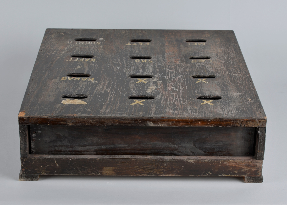 Trekasse for oppbevaring av rasjoneringskort, brukt under og etter andre verdenskrig.
Kassen har en uttrekkbar skuff med flere rom som passer til åpningene i fronten. Håndtaket på skuffen er delvis knust.
Kassen har 12 åpninger i 4 rekker, der det er påmalt tekst: 
1 rekke: X -  X - X 
2 rekke: X - X - kakao
3 rekke: lær - sko - kaffe
4 rekke: mel - fett - sukker