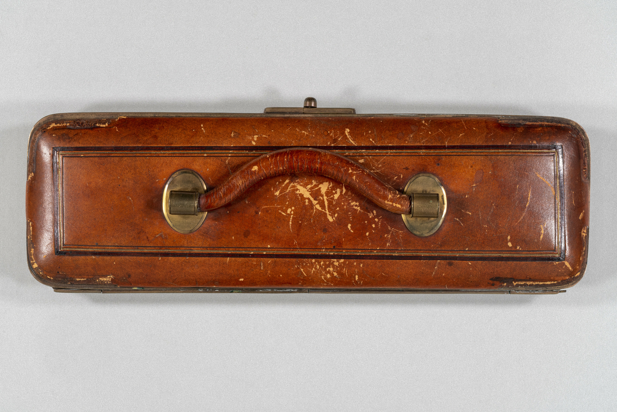 Hanske-etui av skinn, med messingbeslag. Rektangulær form med avrundede hjørner og bunn med belgkonstruksjon. Elfenbens'pren' eller hanskeutvidelsesverktøy med utskjæringer. Inneholder et par hvite, ubrukte skinnhansker med tre knapper på innsiden av håndleddet. Den høyre hansken er revnet oppå hånden og i sidesømmen på begge sider.
Har tilhørt Sara Fabricius.