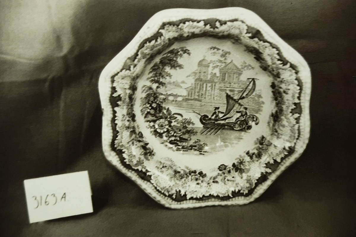 Vaskesett i fajanse, besående av:
A) Vaskevannsfat med sirkulær fotkant med perlebord i relieff. Vid buk med bred blomsterbord. Utbrettet,  8-kantet munningsrand med perlebord langs kanten. Motiv i bunnen: seilbåt med topersoner, hus og bro i bakgrunnen. H: 12.5, Di: 18.5. 

(B) Vaskevannsmugge med sirkulær fotkant, kuleformet buk, sterkt svunget nebb og knekket hank med metallbånd nederst. Dekormotiv i blått, seil med trær og hus på høyre side av buken. Bred blomster-og bladbord innvendig og utvendig ved munningen. H: 29.0, Di:12.5.

(C) Såpekopp, består av to rektangulære 8-kantete deler, begge med blå dekor. Underdelen har blomsterbord langs sidene. Overdelen har gjennomhullet bunn og utoverbrettet munningskant med blå bord. Bunnen har motiv med seilbåt hus og trær. L:12.1, B:8.0, H:5.7. 

(D) Tannbørstebeholder, rektangulær 8-kantet med blå blomsterbord langs sidene. Innvendig to små tugnete tverrvegger til å legge tannbørsten på. L:17.5,B:6.8 H:3.4.