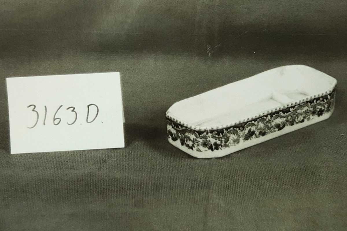 Vaskesett i fajanse, besående av:
A) Vaskevannsfat med sirkulær fotkant med perlebord i relieff. Vid buk med bred blomsterbord. Utbrettet,  8-kantet munningsrand med perlebord langs kanten. Motiv i bunnen: seilbåt med topersoner, hus og bro i bakgrunnen. H: 12.5, Di: 18.5. 

(B) Vaskevannsmugge med sirkulær fotkant, kuleformet buk, sterkt svunget nebb og knekket hank med metallbånd nederst. Dekormotiv i blått, seil med trær og hus på høyre side av buken. Bred blomster-og bladbord innvendig og utvendig ved munningen. H: 29.0, Di:12.5.

(C) Såpekopp, består av to rektangulære 8-kantete deler, begge med blå dekor. Underdelen har blomsterbord langs sidene. Overdelen har gjennomhullet bunn og utoverbrettet munningskant med blå bord. Bunnen har motiv med seilbåt hus og trær. L:12.1, B:8.0, H:5.7. 

(D) Tannbørstebeholder, rektangulær 8-kantet med blå blomsterbord langs sidene. Innvendig to små tugnete tverrvegger til å legge tannbørsten på. L:17.5,B:6.8 H:3.4.