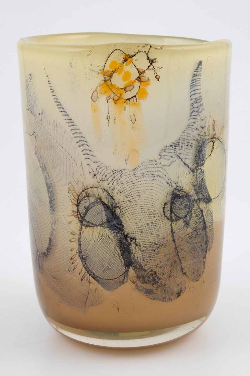 Sylinderformet vase i halvgjennomskinnelig glass. Ujevn munning. Grågrønt underfang som er dekorert med innlagte metalltråder samt partier med finmasket blålig netting. Tidvis brune spetter samt luftbobler i glassmassen. Puntemerke under vasens bunn.