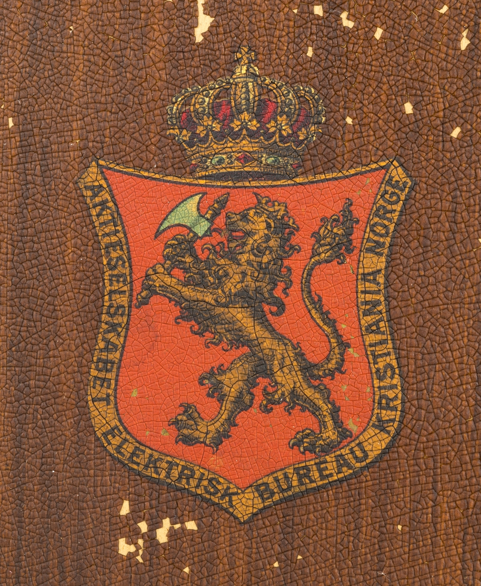 Sveivetelefon, antakelig av type som ble brukt omkring 1. verdenskrig.  Telefonen er montert på ei 1,6 centimeter tjukk treplate.  Apparatet består av ei "kasse" av tre og jernblikk, alt lakkert i edeltreimiterende brunfarge.  I denne delen av apparatet inngår et skrått lokk, en liten skriveklaff, som antakelig skjermer underliggende mekanikk og muligens også batterier.  Ellers har apparatet en forkrommet holder for telefonrøret, som også er forkrommet, men har bakelittkomponenter for håndgrep (midten), øreanlegg og taletrakt.  Apparatet har to omvendt skålformete forkrommete bjeller bak rørholderen, som antakelig gav fra seg klemt når det kom henvendelser per telefon.  Øverst på apparatet er det et slags halvsirkelformet "hode" med informasjon om produsenten.  Her er det også et rødt skjold med en løvefigur med krone over.  Dene logoen finnes også på en svartlakkert, sylindrisk boks på apparatet.  Fra denne boksen er det ledningsforbindelse til stålskiver, som er fastskrudd på begge sider av apparatet. Plata telefonen er montert på har blyantpåskriften «Stor-En-Dammen». Dette antas å være en god indikasjon på at dette apparatet har vært montert i koia ved den nevnte dammen i et av Osensjøens sidevassdrag. Her ble telefonen brukt når fløterne i nedenforliggende deler av vassdraget ønsket å gjøre avtaler som regulerte vanntilførselen i elveløpet på en måte som var optimal ned henblikk på å få tømmeret til å flyte mot Osensjøen.