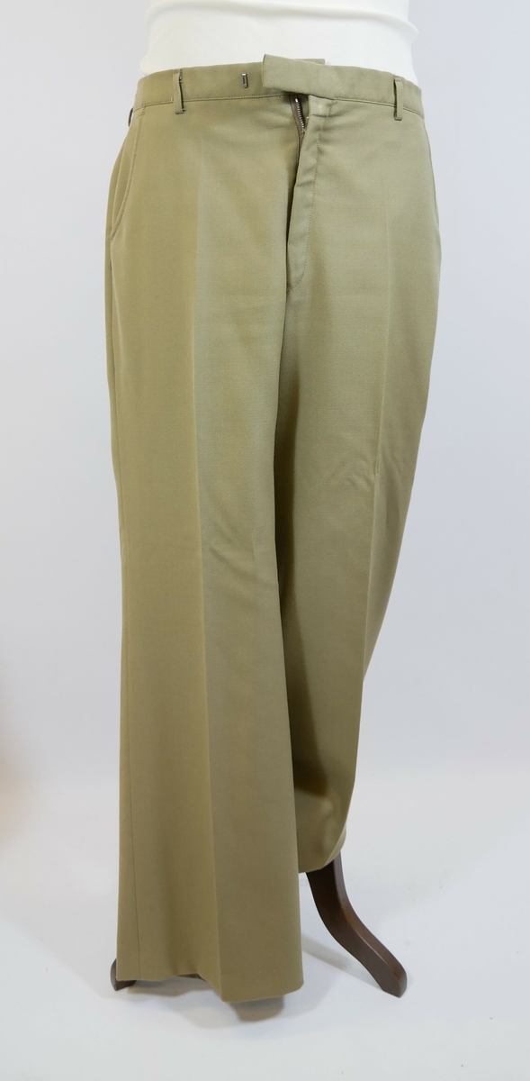 Brun bukse med press. Buksesmekk med glidelås og to metallhekter øverst. To lommer foran og to baklommer. 

Påskrift lapp inne i buksa: 
STYLES BY // KLØVER // 5000 BERGEN
