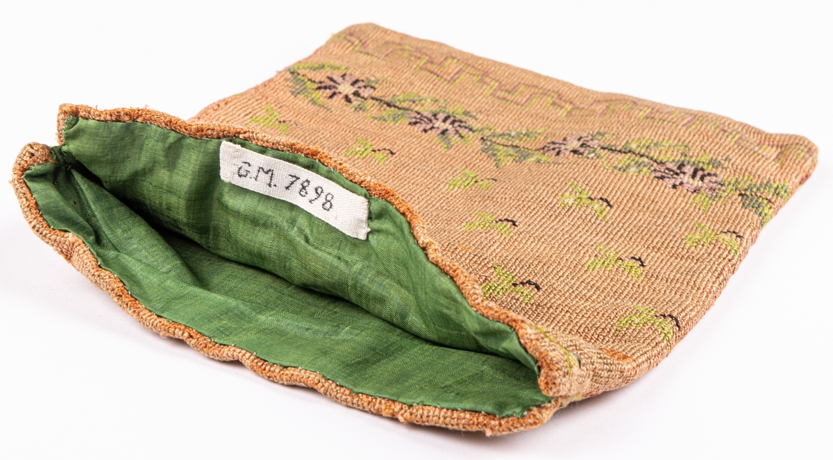 Väska, korsstygnsbroderi i gammalrosa, små blommor och blad strödda, nedtill en ranka i grönt och lila: blommor och blad, nederst en á la greque i grönt och lilka, grönt foder.