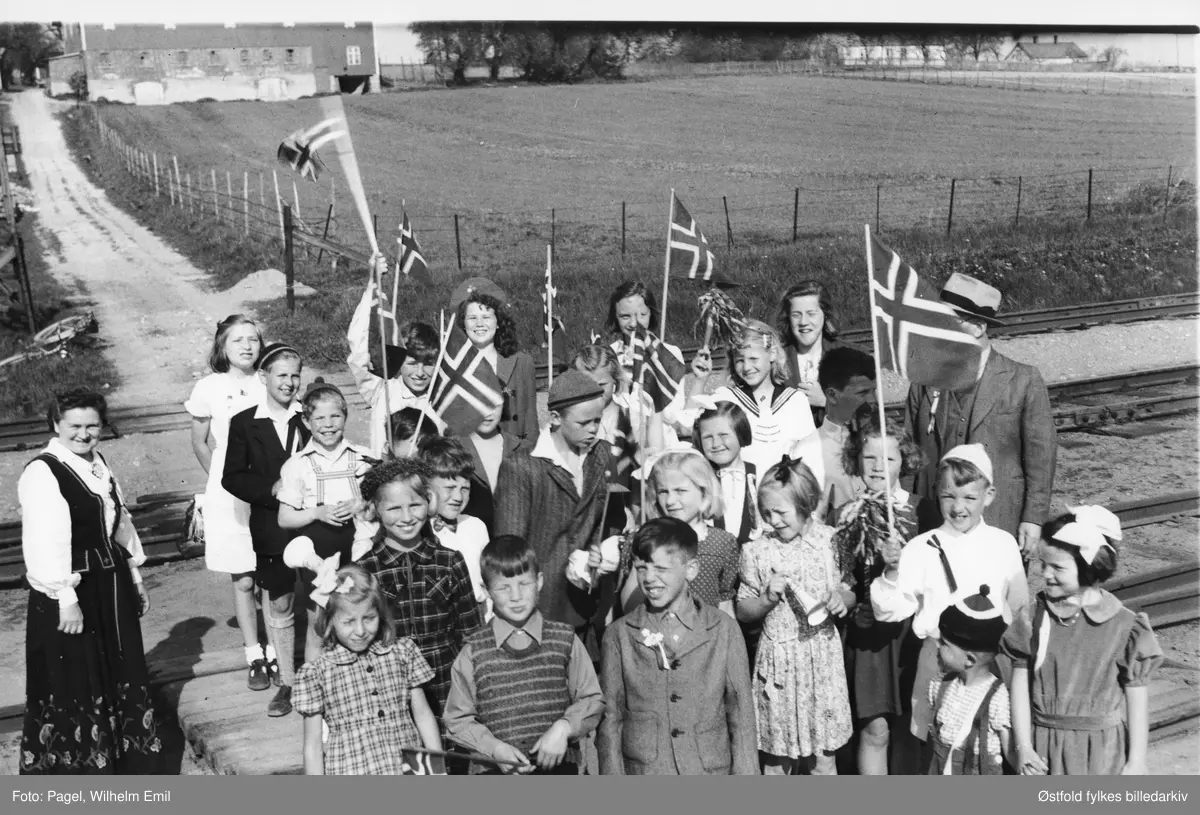 17. mai feiring 1947 for Alvim skole, Brevik jernbaneovergang i Tune. Lite tog med skolebarn fra Alvim skole. Til høyre lærer Per Molland (bak flagg), til venstre fru Molland. Navneliste - snu arket