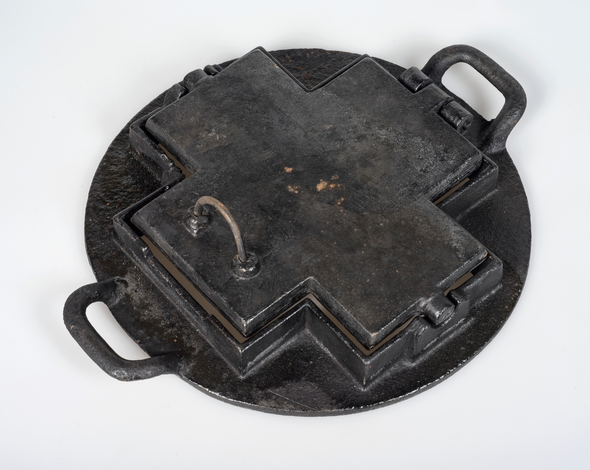 Kakejern med stativ. Jernet er forma som et likearma kryss og kan romme fem kaker om gangen. Stativet er rundt.