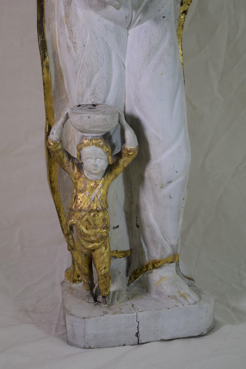 Evangelisten Matteus, stående på høyre ben med engelen ved kneet, oppslått bok på venstre arm. Kappen danner bakgrunn for figuren.