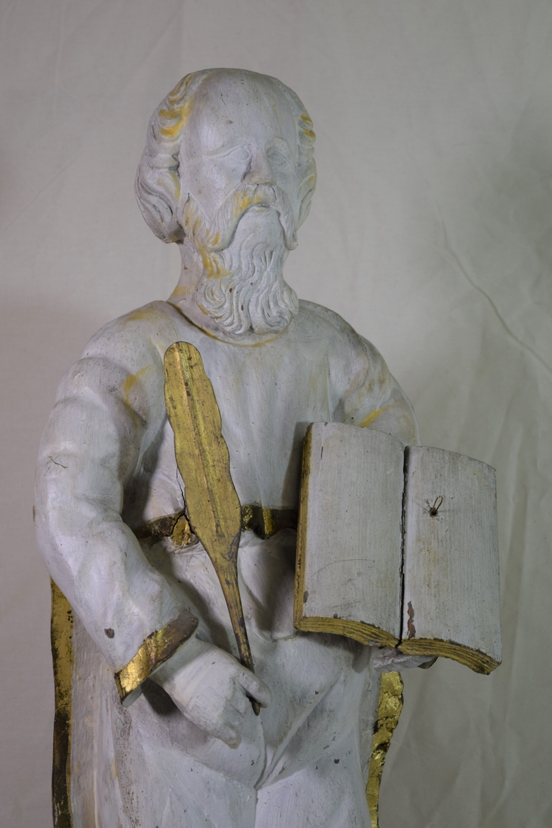 Evangelisten Matteus, stående på høyre ben med engelen ved kneet, oppslått bok på venstre arm. Kappen danner bakgrunn for figuren.