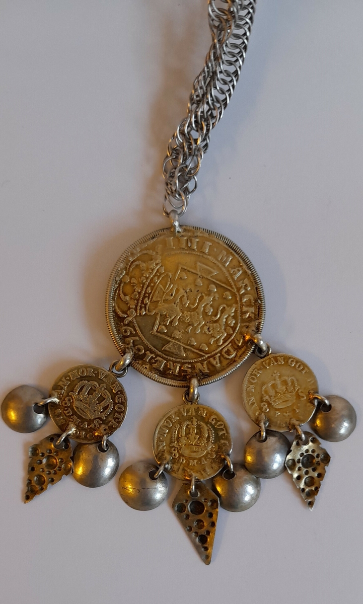 Dalar med kjede.. Frå mynten heng tre mindre myntar med skålar og trekanta lauv.
Mynten har monogram til Christian 5 (1670.1699) og er prega i 1679
Kjedet ligg i eit ovalt hus, trekt med raudt skinn med gulldekor.