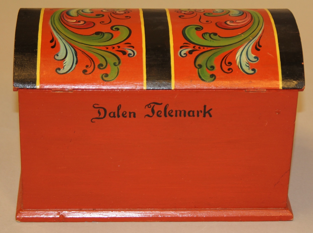 Lita kiste med kuva lok. Rosemåla med tydelege c-krullar. Einsfarga inni, eit lite rom med lok på den eine sida inne i kista.