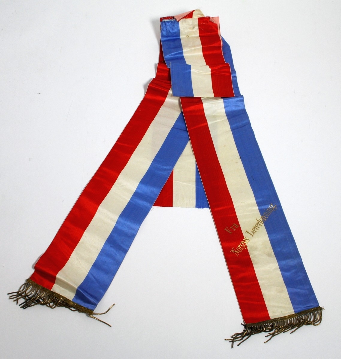 Båresløyfe frå Ivar Aasen si gravferd i 1896. Aasen døydde 23. september 1896, og det var gravferd frå Vår Frelsars gravlund 29. september. (1) På sløyfa står ei helsing "Fra Norges Lærerforening".

Kjelde:
https://www.sprakradet.no/Vi-og-vart/Publikasjoner/Spraaknytt/Arkivet/Spraaknytt_1996/Spraaknytt_1996_1/Om_Ivar_Aasen_i_eit_minneaar/ (Lesedato: 15.10.2020)