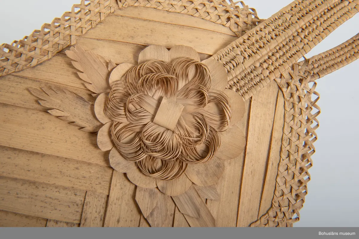 Ur handskrivna katalogen 1957-1958:
Solfjäder av trä, Amerika
Mått: 30 x 18 cm; av bast och tunna träfibrer; en mångsid. platta m. runda hörn, jämte handt. Hel.

Ur handskriven katalog över Uddevalla - Musei Historiska - samlingar: Utländska föremål = De etnografiska föremålen upprättad  år 1916 av Knut Adrian Andersson, Intendent från 1 Oktober 1915:
Solfjäder (Fläkt) av trä (     ), gjord av infödingar å St Barthélèmy 1840talet. Skänkt av fröken Anna Craelius i Uddevalla.

Troligen gjort av strå av någon sorts palmblad.