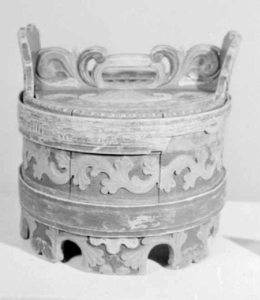 Grønnmalt ambar med to flate grønne gjorder. Mellom dem et felt med skåret og rødmalt akantusbord. Skåret og malt akantusmotiv på føttene - sju intakte og en defekt. Akantus skurd på ørene og skåret lokk med håndtak. Mangler stengsel for lokket. Påmalt innskrift som er slitt og uleselig på et av båndene. Skåret perlerad langs ene kanten.