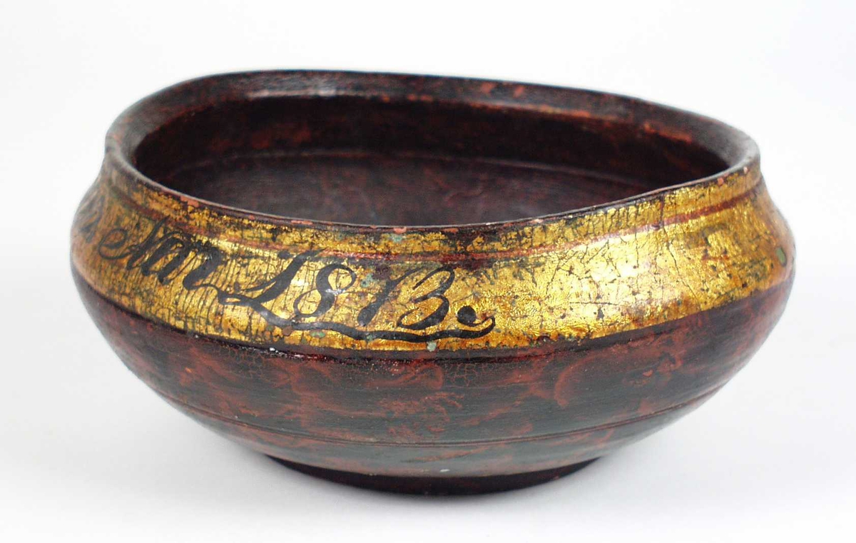 Dreid ølbolle i gran. Krillteknikk er brukt for å få fram det skilpaddelignende mønsteret. Bollen har en gullkant med svart innskrift på. Innvendig har den rød og svart maling.