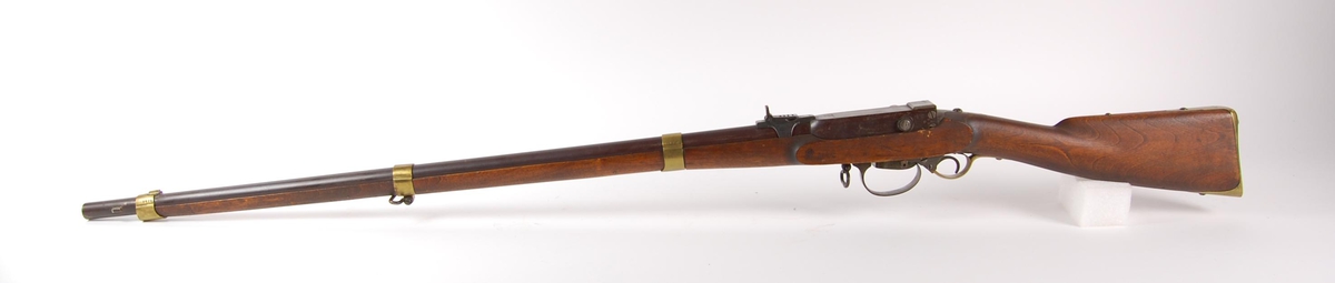 Militært kammerladningsgevær M 1849/55. Rund riflet pipe med militær norsk kammerladningsmekanisme. Kammeret er hengslet i bakkant med hevarm på høyre side. Underliggende hane ( Perkusjonslås ).
Messing bånd, underbeslag, frontsikte og kolbekappe.
(Fint eksemplar)