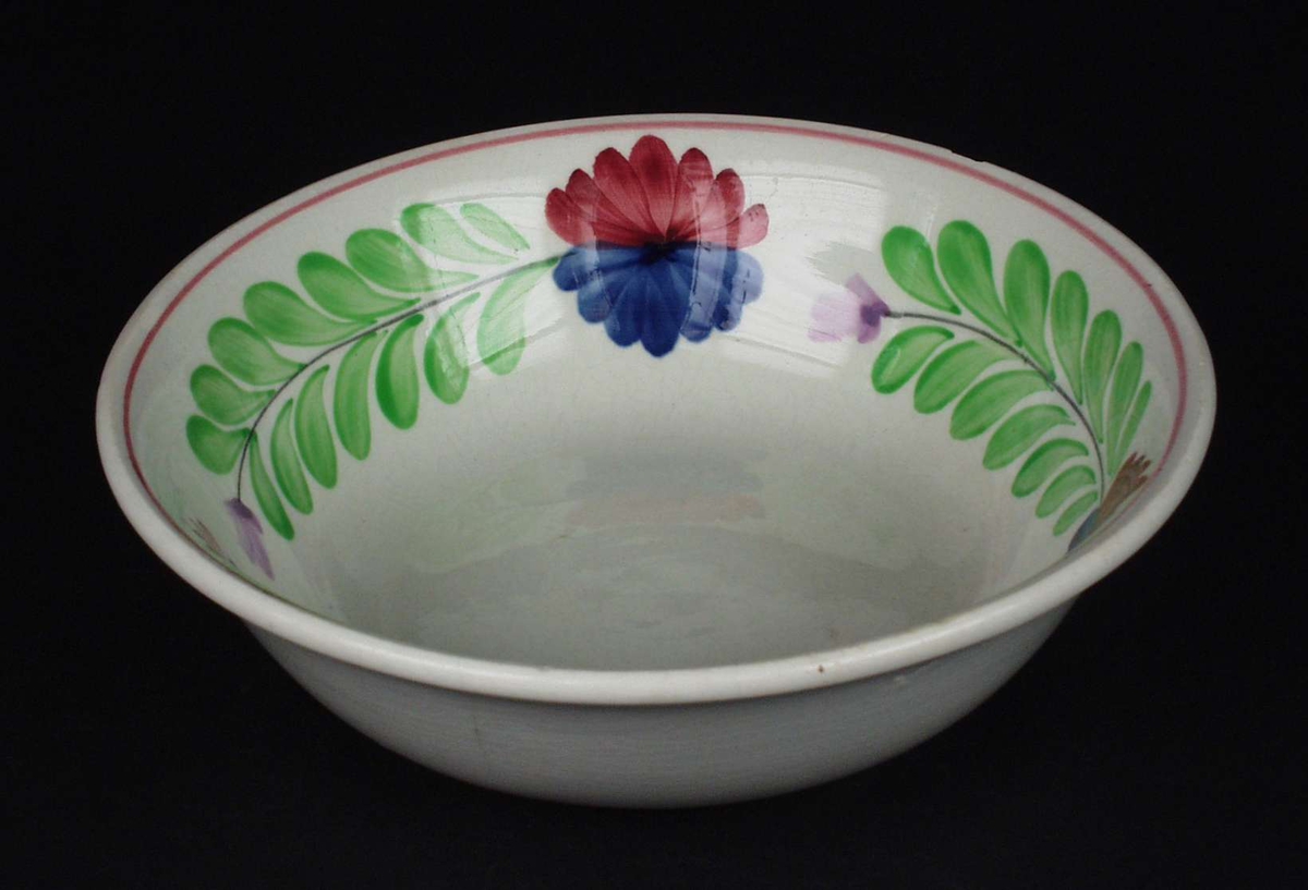 Deler av servise i steintøy og flintgods. Godset er hvitt med malt blomsterdekor. Rød og blå blomst i midten med en ranke av grønne blad.