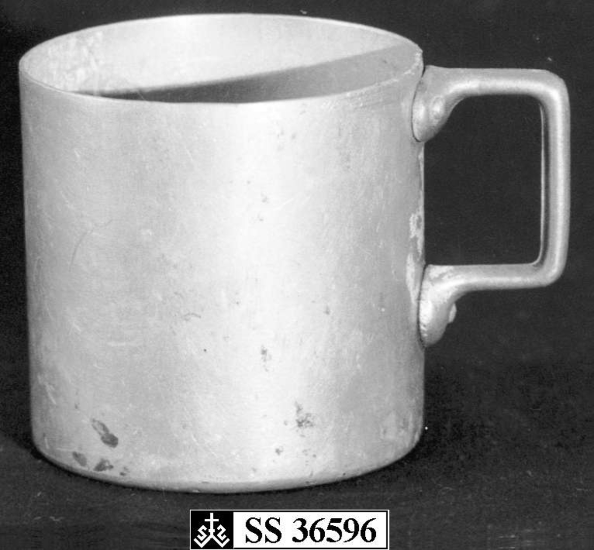 Kopp eller målebeger laget i aluminium. Hanken er naglet fast til koppen.