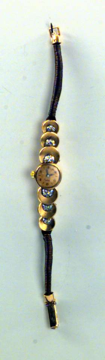 Armbåndsur i gull og kobber. Tallskive med bare like tall. Lenken er antakelig laget av tvunnet kobber. På hver side av urskiven er det tre 'skåler' med stener på, sannsynligvis markasitter.