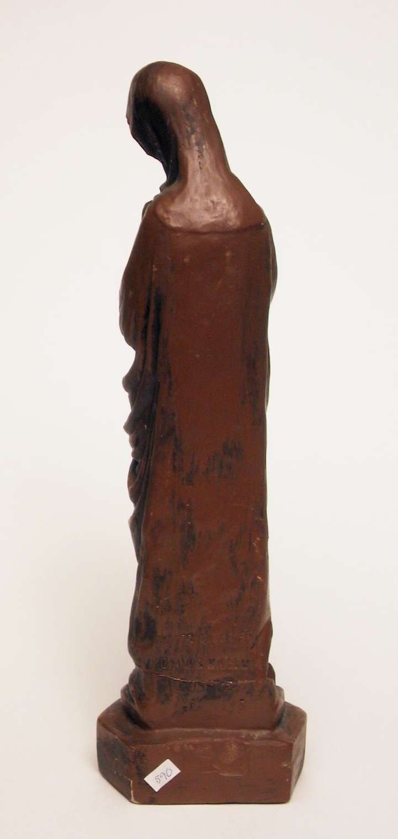 En skulptur av jomfru Maria støpt i gips og malt brun.
Skulpturen har vært slått i to og er limt sammen igjen.