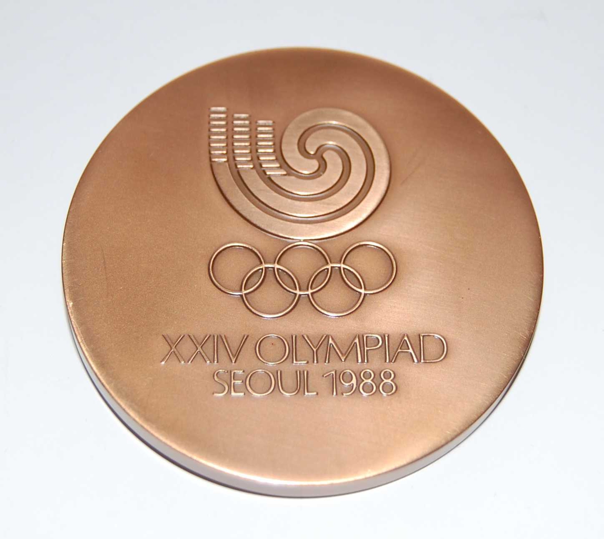 Bronsefarget minnemedalje med emblemet for de olympiske sommerleker i Seoul i 1988 og motiv av Namdaeum, fjelllandskap og fugler.