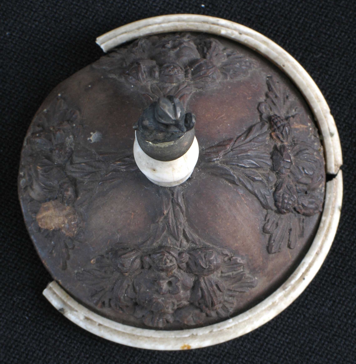 Foten har fire ornamentfelt i relieff, to av dem med blomsterdekor, de to andre med blad og overflødighetshorn. Pokalen bæres av en Neptunfigur utskåret i elfenben, med løftet venstrearm (denne har hatt scepter) og delfin mellom benene. På Neptuns hode en pokal av en kokosnøtt med toppen avskåret som lokk, og med beninnfatning.  Pokalen har relieffutsmykning med nereider og tritoner, som blåser i en koncha (basunlignende instrument). Lokket har fire relieffmotiver med nøtter og to med blomster.  Lokkgrep av ben, balusterformet, med sittende apekatt i metall på toppen.