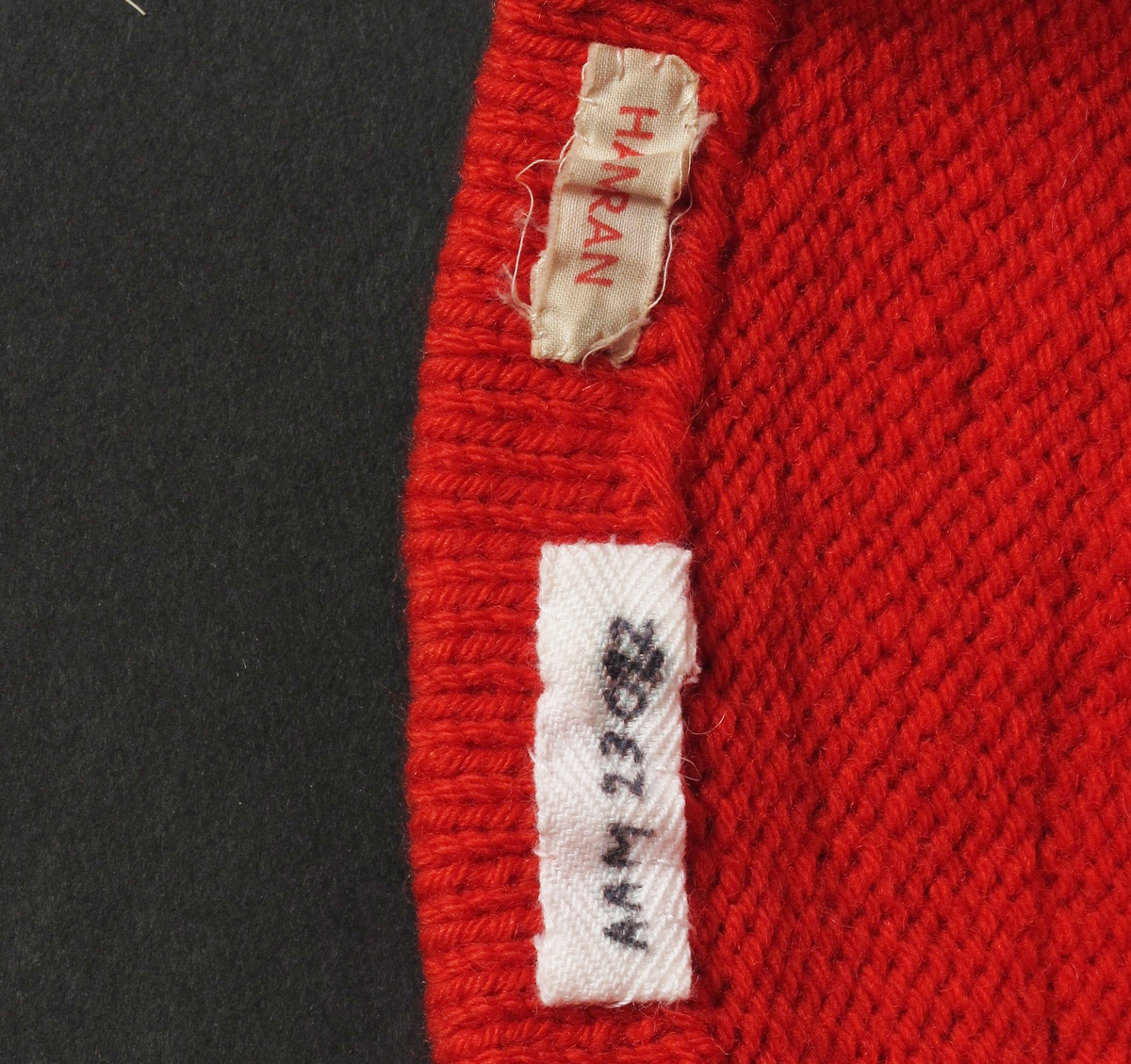 Nisselue, rød topplue.  Ull, rød,  strikket. 
 Barnetopplue,  forholdsvis lang og spiss.  Oppbrettet/fald sydd til med rød tråd.  To rader med fellinger.