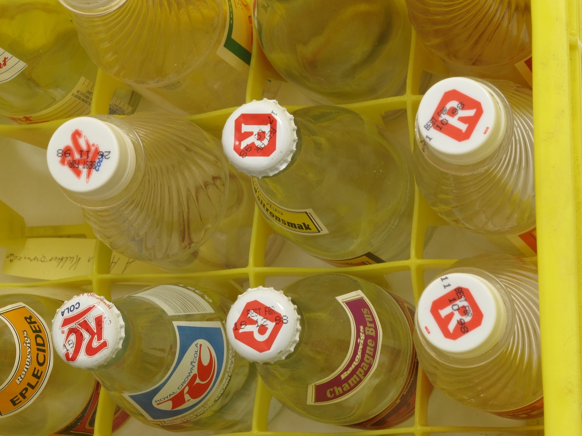 Bruskasse av plast m.rom for 24 flasker. Kassa er full av flasker, assortert utvalg brus fra Rønnevig. Gul kasse med rød skrift.