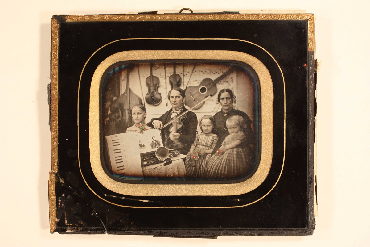 Gruppeportrett av organist Thoschlag  i Arendal med familie, 1852. Mot bakgrunn av musikalier ser man Friedrich Wilhelm  Thoschlag, stadsmusikus i Arendal, og hans hustru  Birgitte Rosina Hachenberg med tre barn: fra v.  døtrene Felicita f. 1842, Birgitte Wilhelmine Camilla  f. 1846, og Betty Cecilie Jenny f. 1849.  Barna holder små malte blomsterbuketter i hendene. 