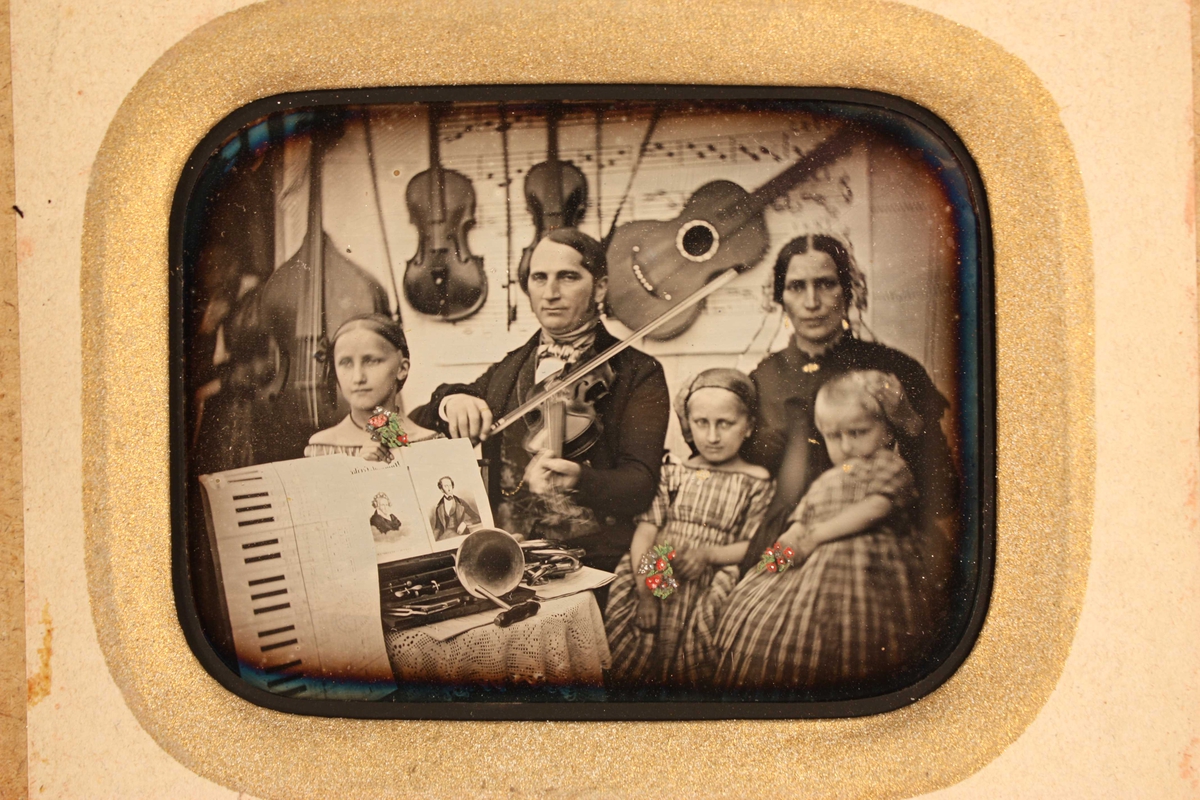 Gruppeportrett av organist Thoschlag  i Arendal med familie, 1852. Mot bakgrunn av musikalier ser man Friedrich Wilhelm  Thoschlag, stadsmusikus i Arendal, og hans hustru  Birgitte Rosina Hachenberg med tre barn: fra v.  døtrene Felicita f. 1842, Birgitte Wilhelmine Camilla  f. 1846, og Betty Cecilie Jenny f. 1849.  Barna holder små malte blomsterbuketter i hendene. 