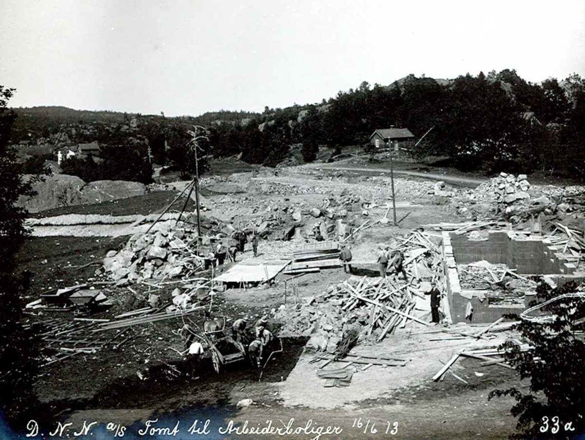 "16/06-1913" Eydehavn. Utgraving og grunnarbeider for tomter til arbeiderboliger i Nesgaten. Uthuset til høyre tilhørte Mari og Kittel Næs, som bodde like til høyre. Det er fortalt at til et arbeidslag hørt 12-15 mann pluss hest og kjerre.
