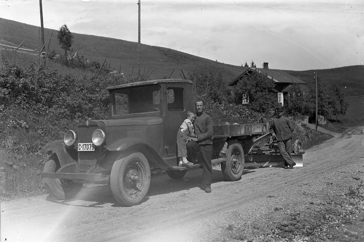 Lastebil med veiskrape - sannsynligvis Akershus Fylkes Vegvesen på vei ned mot Bønsdalen. Nils Nordheim med sønnen Ragnar. Eilif Gundersen bak. Tatt ved Granly gård. Lastebilen er en Chevrolet 1929-30