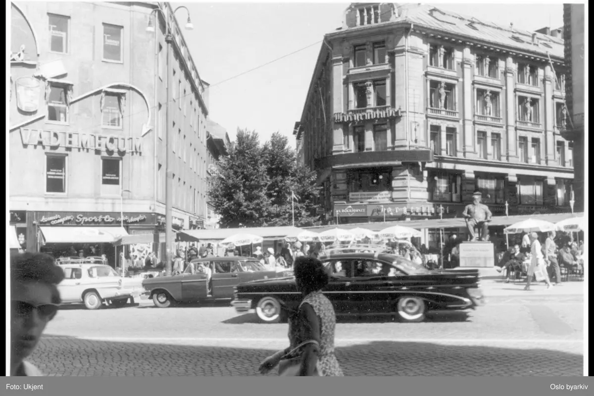 Trafikkmiljø i Karl Johans gate foran Stortings plass. Uteservering under Christian Krohg-statuen. Centralgården (Morgenbladgården) bak til høyre. Brambanigården til venstre med reklame for "vademecum".Arbeidergata bak i midten.