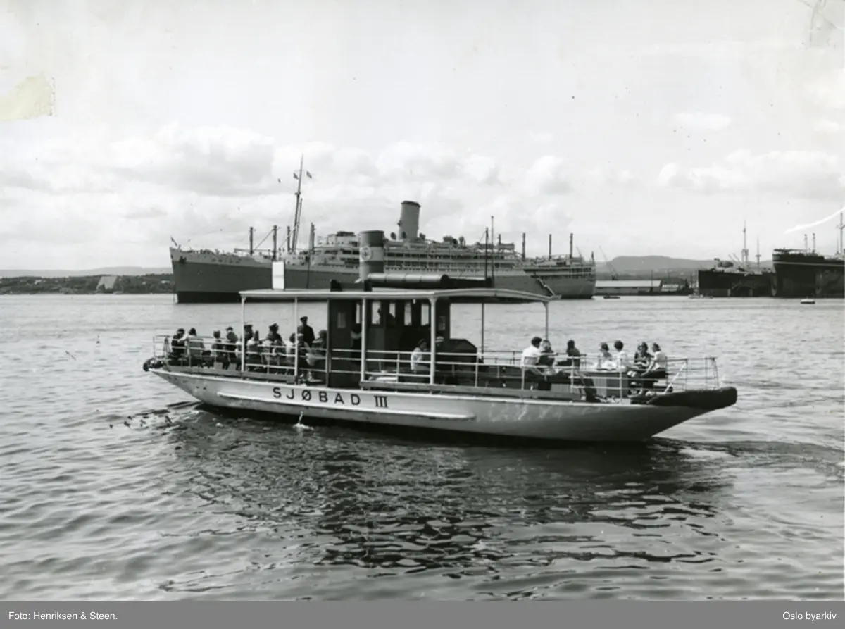 Oslo kommunale badefrege, Sjøbad III på vei ut fra Rådhuskaia ved Akershusstranda i Pipervika, på vei til en av øyene ute i fjorden. Passasjerskipet Orion til ankers utenfor dokkanlegget til Aker mekaniske verksted. Frammuseet på Bygdøy helt i bakgrunnen.